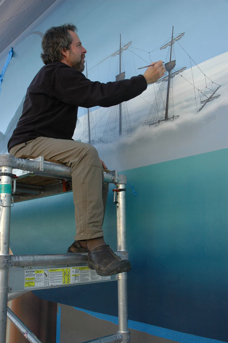 trompe l'oeil muralist john pugh painting a ship on scaffolding for a mural in santa cruz